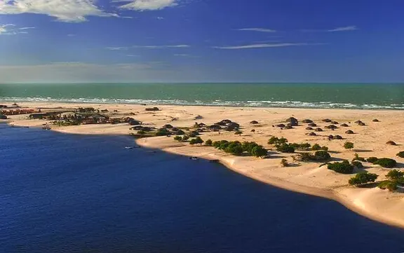 Faixa de areia com vegetação separando o rio do mar