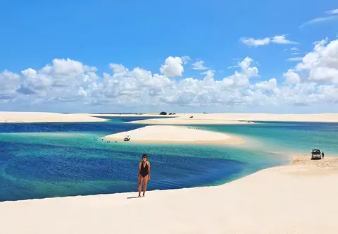 Turista à beira de uma lagoa azul cercada de dunas brancas