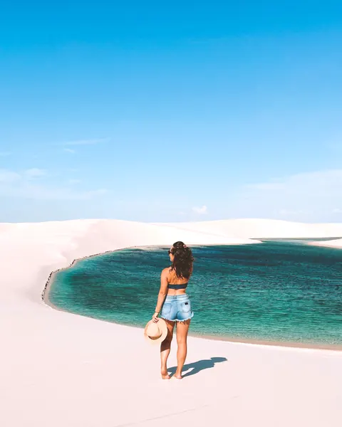 Turista em pé na areia diante de uma lagoa verde entre dunas
