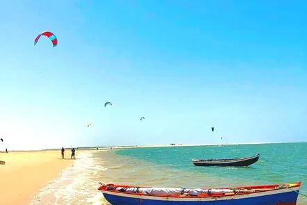 Praia com barcos de pesca na areia e kitesurf ao fundo