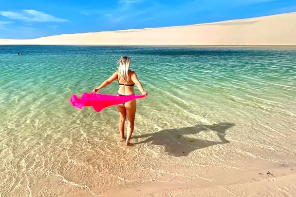 Turista caminhando em lagoa de água cristalina segurando um lenço rosa