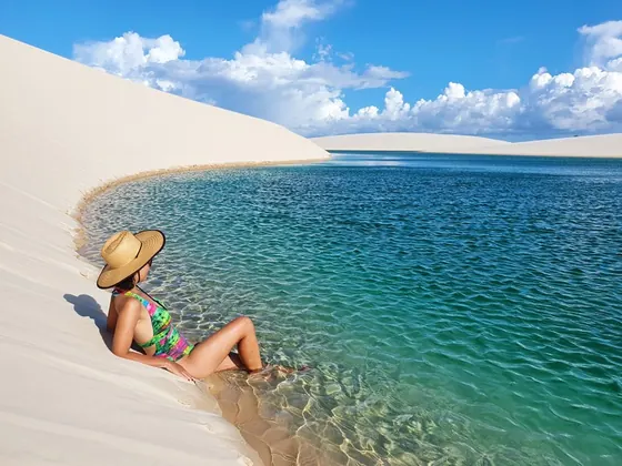 Turista de chapéu sentada à beira de uma lagoa azul entre as dunas