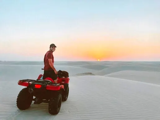 Turista sobre um quadriciclo vermelho nas dunas ao entardecer